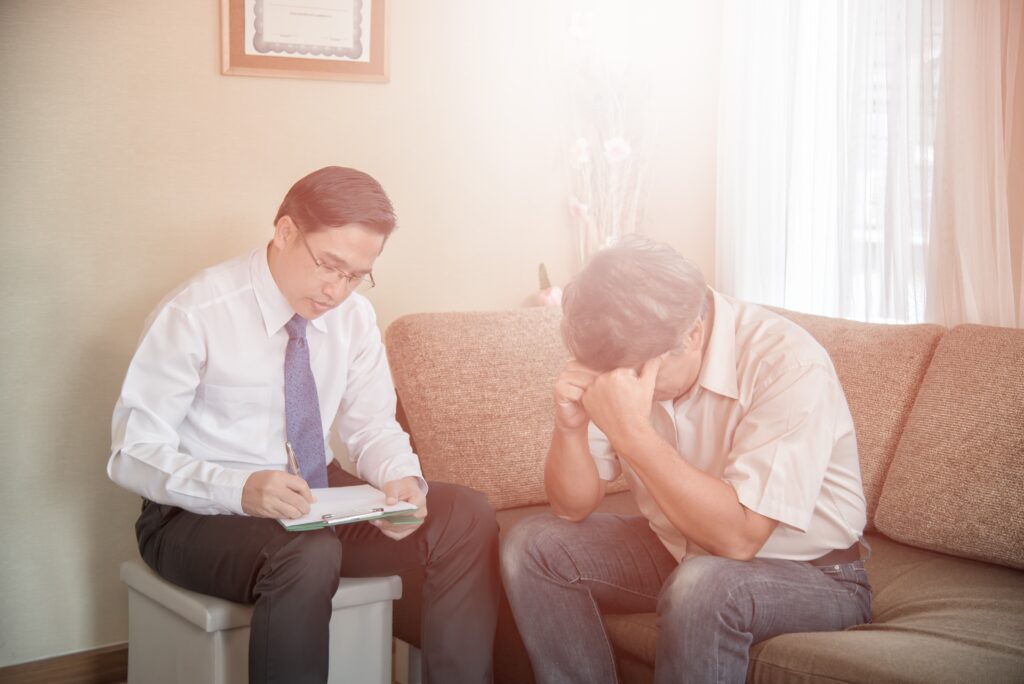 a man gives advice while another man sits on a couch holding his head in his hands